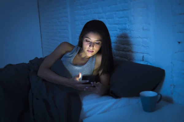 Chica en la cama usando el teléfono móvil tarde en la noche en dormitorio oscuro acostado feliz y relajado — Foto de Stock