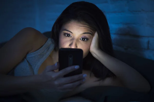 Chica en la cama usando el teléfono móvil tarde en la noche en dormitorio oscuro acostado feliz y relajado —  Fotos de Stock