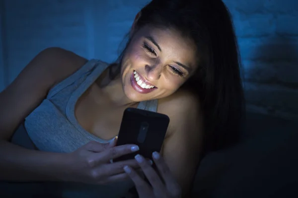 Девушка в постели с помощью мобильного телефона поздно ночью в темной спальне лежал счастливым и расслабленным — стоковое фото