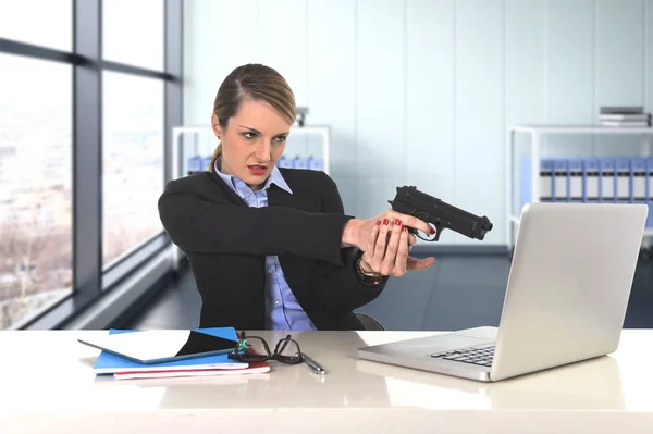 Mujer de negocios apuntando arma a la computadora portátil sentado en el escritorio desesperado y estresado —  Fotos de Stock