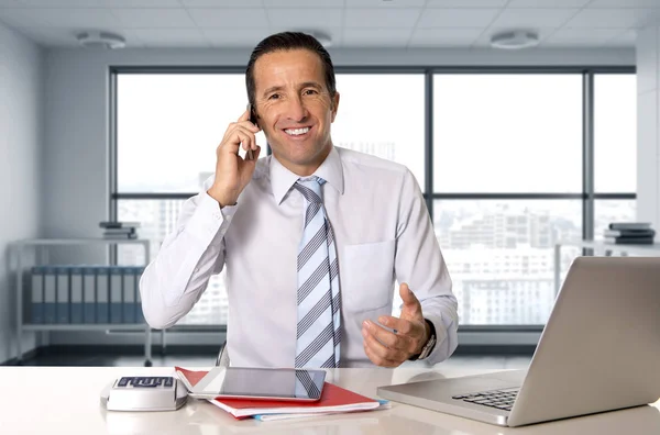Homem de negócios feliz que trabalha no computador portátil que fala no telefone móvel no escritório — Fotografia de Stock