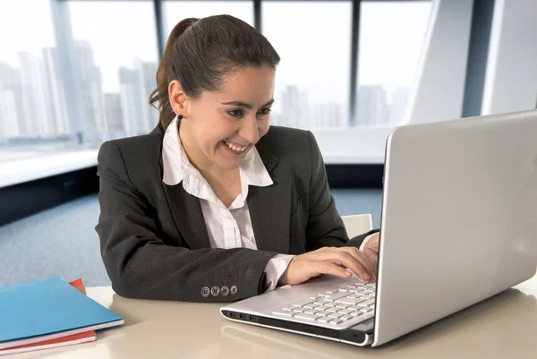 Empresária sorrindo feliz vestindo um terno de negócios trabalhando em seu computador portátil na sala de escritório moderna — Fotografia de Stock