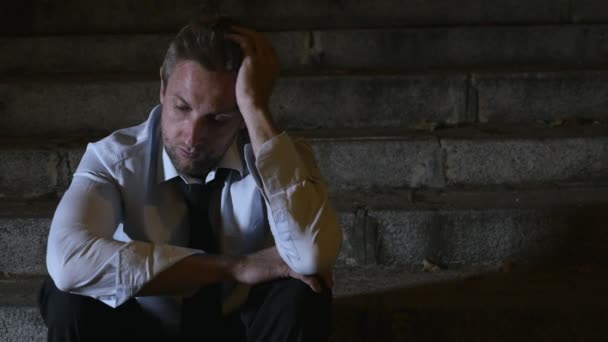 4K відео бічна панорама 24 кадри молодого відчайдушного бізнесмена в костюмі і краватці страждають стресом і депресією, сидячи на міських вуличних сходах вночі сумно і стурбовані концепцією кризової рецесії — стокове відео