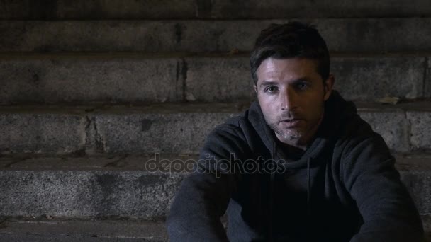 4K video lateral panning 24 fps of young desperate wasted man in hood suffering stress and drepression sitting miserable on urban street staircase at night sad and worried in addiction concept — Stock Video