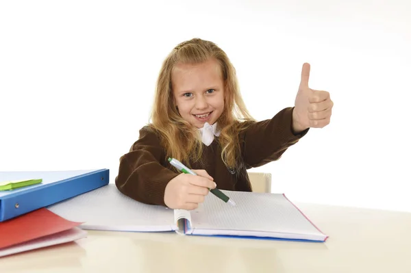 Vackra Skolflicka i skoluniform som med blont hår leende glad sitter på skrivbord gör läxor — Stockfoto