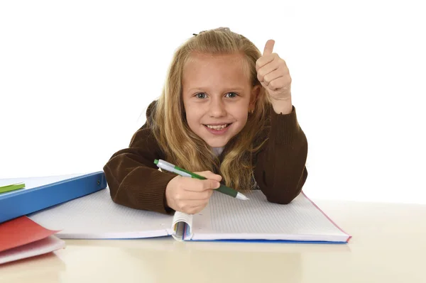 Beautiful schoolgirl in school uniform with blond hair smiling happy sitting on desk doing homework — Stock Photo, Image