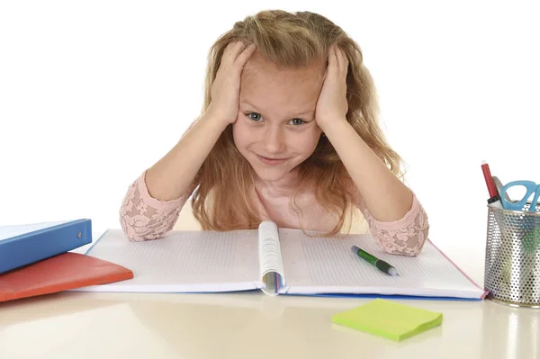 Красивая школьница с светлыми волосами улыбается счастливо сидя на столе делать домашнее задание изолированы на белом — стоковое фото