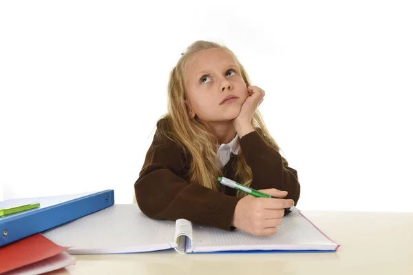 Colegiala en uniforme escolar sentada en el escritorio de estudio haciendo la tarea buscando mente reflexiva y ausente — Foto de Stock