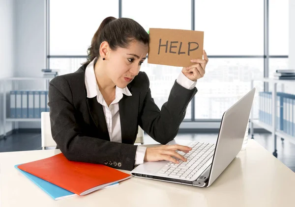 Mujer vistiendo un traje de negocios trabajando en su computadora portátil sosteniendo un cartel de ayuda sentado en la oficina moderna —  Fotos de Stock