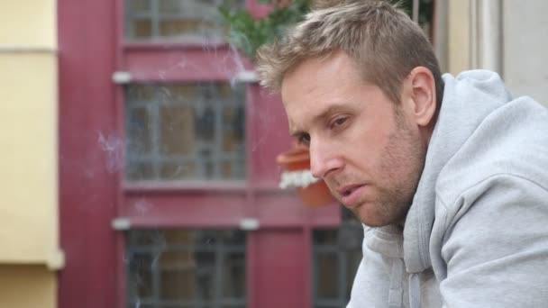 4k 24 fps video de mano leva de cerca joven triste hombre en el balcón mirando a la distancia triste y deprimido fumar cigarrillo enojado y desesperado en concepto de depresión y problemas — Vídeo de stock