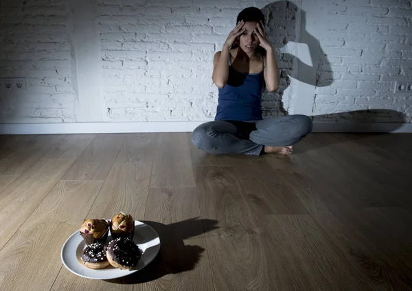 Beignets de sucre malsains et muffins et tentés jeune femme ou adolescente assise sur le sol — Photo