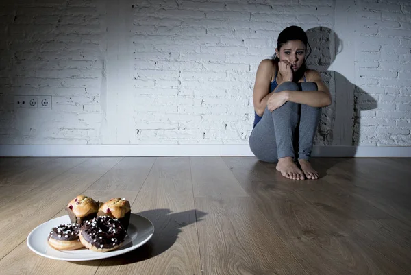 Ciambelle e muffin allo zucchero malsani e giovane donna tentata o adolescente seduta a terra — Foto Stock