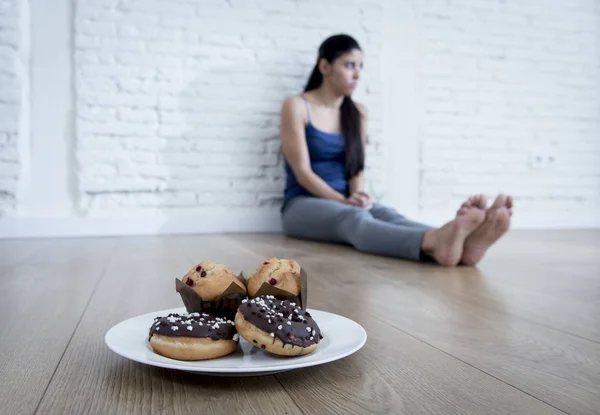 Donuts açúcar insalubres e muffins e tentada jovem mulher ou adolescente sentada no chão — Fotografia de Stock