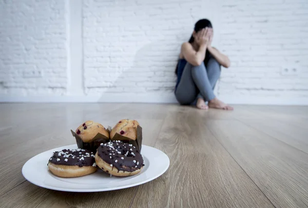 Rosquillas y magdalenas de azúcar poco saludables y joven tentada o adolescente sentada en el suelo — Foto de Stock