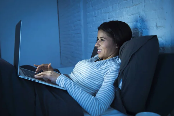 Νεαρή όμορφη γυναίκα Ισπανόφωνος στο κρεβάτι στο σπίτι γελάει ευτυχισμένος στον φορητό υπολογιστή τη νύχτα — Φωτογραφία Αρχείου