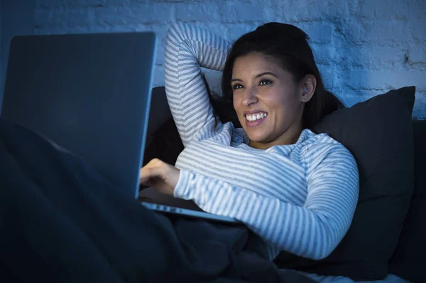 Νεαρή όμορφη γυναίκα Ισπανόφωνος στο κρεβάτι στο σπίτι εργασίας ευτυχισμένος στον φορητό υπολογιστή τη νύχτα — Φωτογραφία Αρχείου