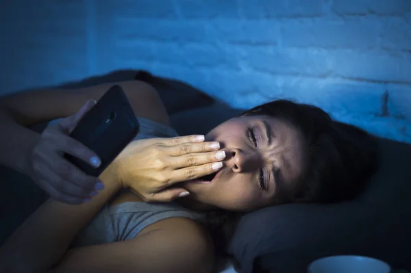 Mujer latina en la cama tarde en la noche mensajes de texto utilizando el teléfono móvil bostezando soñoliento y cansado — Foto de Stock