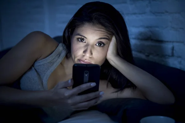Jeune belle femme latine sur le lit tard dans la nuit textos en utilisant le téléphone mobile somnolent et fatigué — Photo
