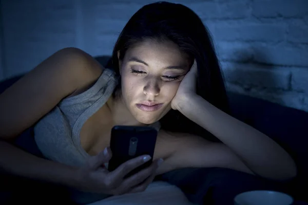 Jeune belle femme latine sur le lit tard dans la nuit textos en utilisant le téléphone mobile somnolent et fatigué — Photo