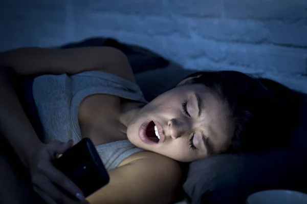 Mujer latina en la cama tarde en la noche mensajes de texto utilizando el teléfono móvil bostezando soñoliento y cansado —  Fotos de Stock