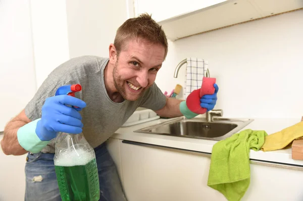 Młody człowiek szczęśliwy w gumowe rękawice gospodarstwa detergent czyszczący spray i gąbki, uśmiechając się do prania — Zdjęcie stockowe