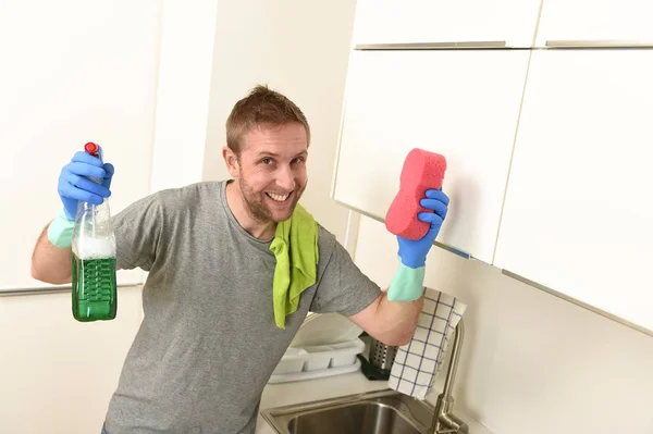 Młody człowiek szczęśliwy w gumowe rękawice gospodarstwa detergent czyszczący spray i gąbki, uśmiechając się do prania — Zdjęcie stockowe