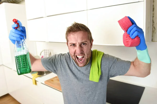 Joven hombre sosteniendo limpieza detergente spray y esponja lavado casa cocina limpia enojado en el estrés — Foto de Stock