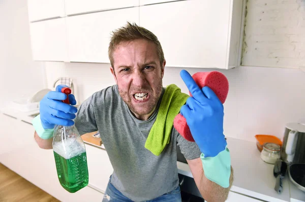 Joven hombre sosteniendo limpieza detergente spray y esponja lavado casa cocina limpia enojado en el estrés — Foto de Stock