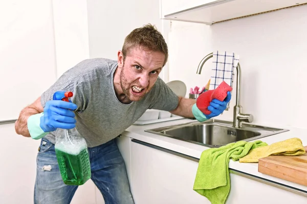 Joven hombre sosteniendo limpieza detergente spray y esponja lavado casa cocina limpia enojado en el estrés — Foto de Stock