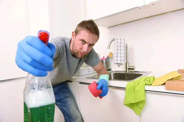 Young man holding cleaning detergent spray and sponge washing home kitchen clean angry in stress — Stock Photo, Image