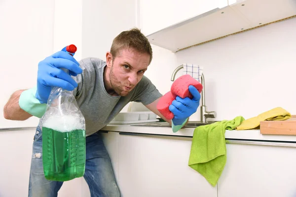 Молодий чоловік тримає миючий засіб спрей і губку миття домашньої кухні чистий сердитий стрес — стокове фото