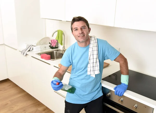 Joven feliz hombre sosteniendo la botella detergente lavado spray y tela en guantes de goma sonriendo — Foto de Stock