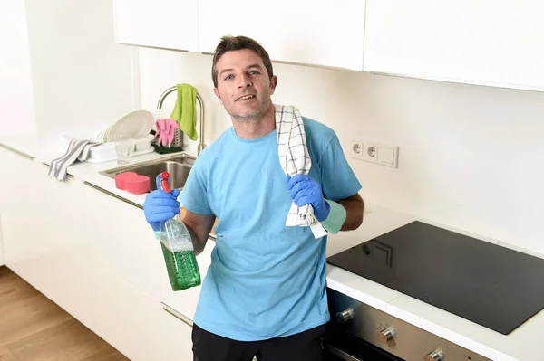 Молодий щасливий чоловік тримає пляшку миючого засобу для розпилення і тканину в гумових рукавичках посміхаючись — стокове фото