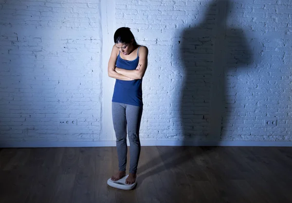 Muda fit dan ramping wanita memeriksa berat badan pada skala dengan besar bayangan tegang cahaya sedih dan putus asa — Stok Foto