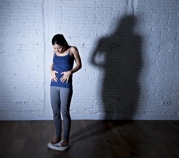 Молодая стройная женщина проверяет вес тела по шкале с большим ярким теневым светом грустным и отчаянным — стоковое фото