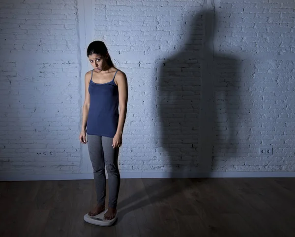 Молодая стройная женщина проверяет вес тела по шкале с большим ярким теневым светом грустным и отчаянным — стоковое фото