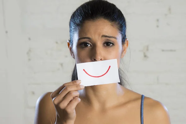 Joven hermosa mujer deprimida ocultando su dolor y tristeza detrás de un papel con una sonrisa dibujada — Foto de Stock