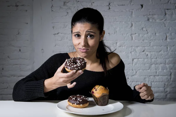 Mujer sentada en la mesa sintiéndose culpable olvidando dieta comiendo plato lleno de comida chatarra azucarada poco saludable — Foto de Stock