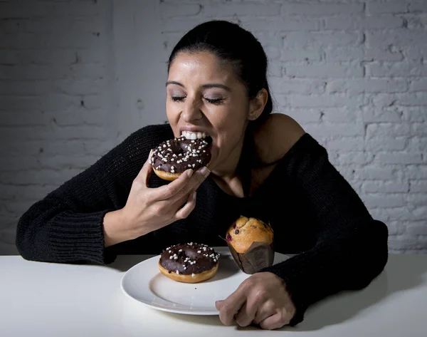 Joven atractiva latina sentada a la mesa comiendo plato lleno de comida chatarra azucarada poco saludable —  Fotos de Stock