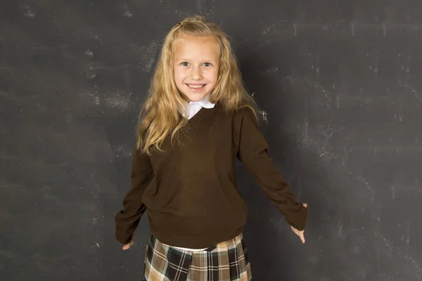 Süßes Schulmädchen in Uniform lacht aufgeregt vor Schultafel und lächelt glücklich — Stockfoto