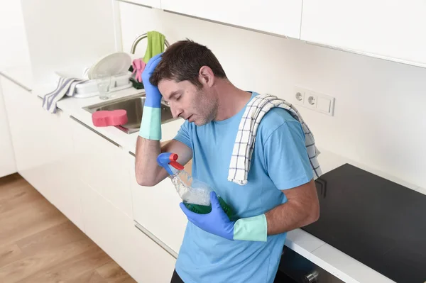 Молодой ленивый уборщик дома моет и чистит кухню бутылкой с моющим средством — стоковое фото