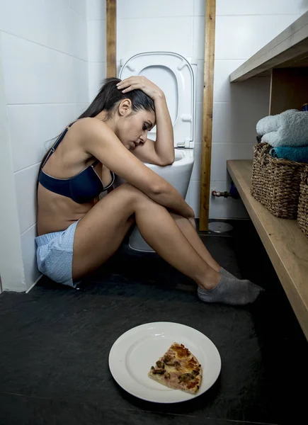 Молодая грустная и подавленная булимия женщина чувствует себя виноватой после рвоты пиццы в унитазе — стоковое фото