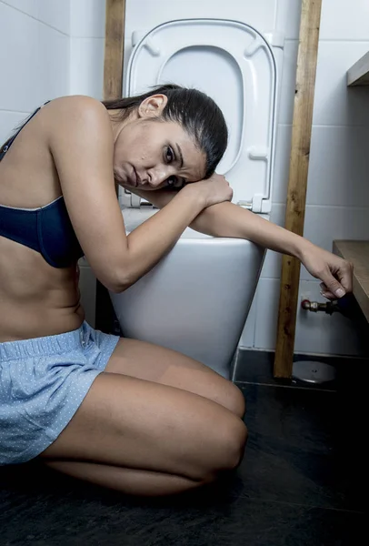 Joven mujer bulímica triste y deprimida sintiéndose enferma sentada en el suelo del inodoro apoyada en el WC — Foto de Stock