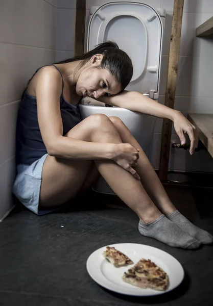 Молодая грустная и подавленная булимия женщина чувствует себя виноватой после рвоты пиццы в унитазе — стоковое фото