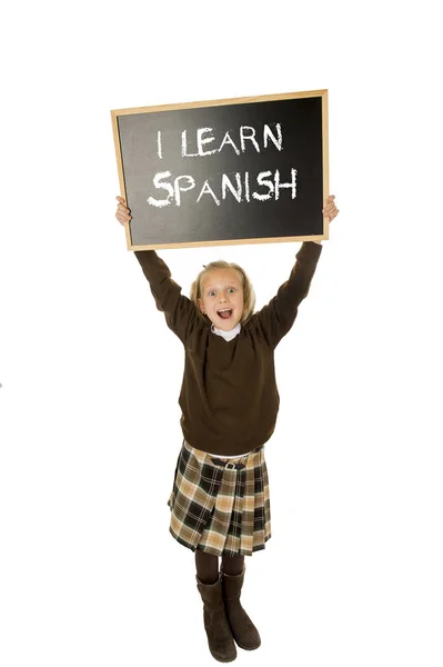Gadis sekolah tersenyum bahagia dan gembira memegang dan menunjukkan papan tulis kecil dengan teks aku belajar bahasa Spanyol — Stok Foto