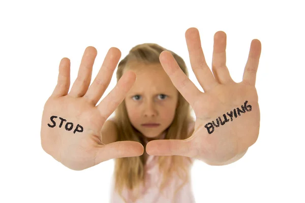 Zoet en bang weinig schoolmeisje met de tekst stop pesten geschreven in haar handen — Stockfoto