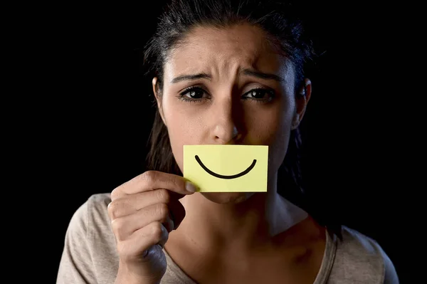 Латиноамериканская грустная депрессивная латиноамериканка держит бумагу, прикрывая рот фальшивой нарисованной улыбкой — стоковое фото