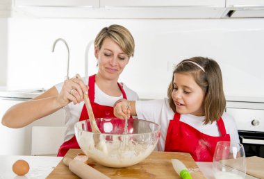 genç anne ve aşçı önlüğü birlikte modern ev mutfak pişirme pişirmek küçük tatlı kız