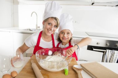 genç anne ve küçük tatlı kızı aşçı şapkası ve birlikte evde mutfak pişirme yemek önlük