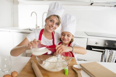 genç anne ve küçük tatlı kızı aşçı şapkası ve birlikte evde mutfak pişirme yemek önlük